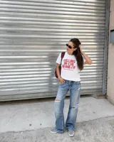 Remera blanca de manga corta, con cuello redondo y diseño estampado en el centro con la frase "Killing in the name of" en color rojo.