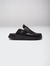 Zuecos de cuero color suela con diseño de punta redonda y ajuste mediante una tira con hebilla metálica en el empeine. Presentan una suela plana de goma negra y plantilla interior con logo grabado.