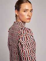 Blusa de viscosa con estampado geométrico en tonos blanco, rojo, negro y marrón. Presenta cuello subido, mangas largas abullonadas con frunces en los hombros y puños elásticos.