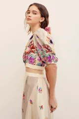 Top corto cruzado de viscosa con escote en V, mangas cortas abullonadas y diseño estampado con flores multicolores sobre fondo beige.
