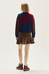 Polera de tejido de punto con diseño multicolor que combina rayas horizontales en tonos azul y bordó, flecos decorativos en el frente y un bordado central en forma de trenza. Presenta cuello semi polera, mangas largas y puños acanalados.