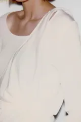 Camiseta de manga larga color crudo con cuello redondo y detalle de top halter superpuesto en el mismo tejido. Presenta un diseño de doble capa con caída drapeada en el frente.