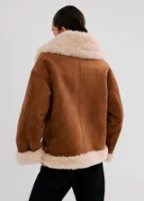 Chaqueta estilo aviador de ante sintético en color marrón con detalles de borrego sintético en el cuello, los puños, la solapa y el dobladillo inferior, con bolsillos laterales y cierre frontal con cremallera.