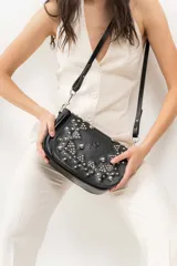 Bandolera de cuero negro con estructura rígida, tapa frontal decorada con tachas metálicas plateadas colocadas a mano y correa larga ajustable.