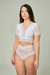 Conjunto de lencería blanco compuesto por un corpiño corto con mangas cortas y detalles de encaje floral en el escote y bajo busto, y una bombacha hipster tiro alto completamente de encaje.