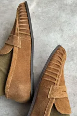 Mocasín de cuero marrón con textura croco y acabado brillante, de diseño clásico con detalle de antifaz en el empeine y costuras pespunteadas alrededor de la puntera.