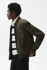 Campera bomber de color verde militar, con cuello elevado acanalado, cierre frontal, bolsillos laterales con cierre y ribetes acanalados en puños y bajo.