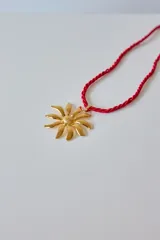 Collar con tiento trenzado blanco y dije metálico dorado con forma de sol estilizado.