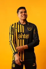 Camiseta de f&uacute;tbol Puma del Club Atl&eacute;tico Pe&ntilde;arol, modelo Aniversario de manga larga. Dise&ntilde;o combinado con la mitad derecha a rayas verticales amarillas y negras, y la mitad izquierda totalmente negra con detalles en amarillo.