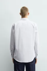 Camisa de corte regular fit confeccionada en tejido de algodón con diseño de rayas verticales finas. Presenta cuello italiano, manga larga con puños abotonados y cierre frontal mediante botonadura.