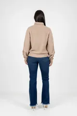 Buzo de tejido de punto texturizado en color camel, con cuello alto y detalle de botones decorativos metálicos en los hombros. Presenta mangas largas con puños ajustados y un corte relajado.