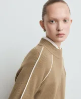 Jersey de punto color tostado con cuello alto y mangas raglán con líneas blancas decorativas en los hombros.
