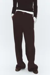 Pantalón negro de tiro alto, con trabillas, bolsillos laterales y de vivo en la espalda. Presenta pliegues en el delantero y cierre frontal con botón.