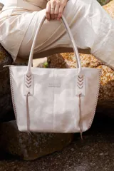 Cartera tote bag de cuero vacuno color negro, con detalles de trenzado lateral en contraste con flecos, asas largas de hombro y compartimento amplio con bolsillo interior.