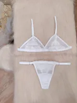 Conjunto de lencería compuesto por un corpiño triangular de microtul transparente con detalles de encaje floral en las copas y una tanga regulable con elástico ancho.