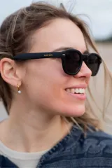 Lentes de sol con armazón negro mate y cristales oscuros, de diseño clásico y versátil con la inscripción de la marca en la patilla.