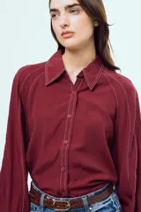 Camisa bordó de manga larga abullonada, con costuras en contraste color blanco, cuello camisero y cierre frontal de botones.
