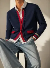 Chaqueta de punto tipo cardigan color azul marino, con detalles en rojo en la botonadura frontal, bolsillos y puños. Presenta un diseño con volados en los bordes frontales, botones dorados y puños con franjas en tonos beige y rojo.