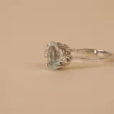 Anillo solitario de oro blanco 18k con una piedra central de aguamarina en corte ovalado y pequeños brillantes laterales engarzados en cuatro puntas.