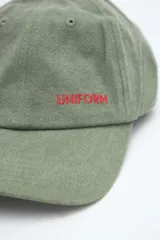 Gorra verde militar de diseño clásico con visera curva y bordado frontal en hilo rojo con la palabra "UNIFORM".