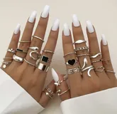 Set de 27 anillos plateados con diferentes diseños: lisos, con forma de serpiente, con corazones, con piedras negras, con forma de mariposa y con eslabones.