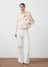Chaqueta crop de lino color beige, diseño recto, cuello alto tipo embudo, manga larga, dos bolsillos laterales y cierre cruzado de doble botonadura metálica dorada con detalles en los hombros.