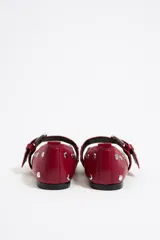 Bailarinas negras de cuero con punta fina, tachas plateadas y correa con hebilla metálica. Zapato plano con suela fina.