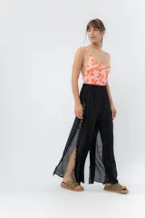 Pantalón ancho de gasa liviana color negro, con aberturas laterales altas decoradas con pompones negros.