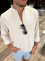 Camisola de lino color beige, con cuello mao y cierre frontal parcial con botones. Presenta mangas largas con puños arremangados y un corte holgado.