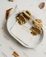 Par de aros colgantes dorados con cuatro dijes metálicos móviles con forma de hojas o gotas brillantes. Fabricados en acero quirúrgico con baño de oro.
