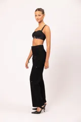 Top tipo corset negro con copas armadas y diseño drapeado en el busto. Presenta una base curva decorada con ojalillos metálicos y tachas plateadas. Incluye breteles intercambiables y cierre posterior con ganchos regulables.