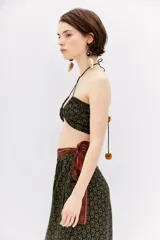 Top crop estilo bandeau con escote fruncido y tirantes finos cruzados en la espalda. Confeccionado en tela estampada con diseño floral en tonos mostaza, verde y terracota sobre fondo negro.