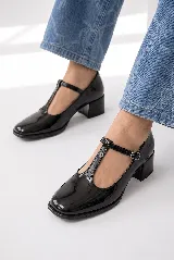 Zapatos de tacón bajo tipo Mary Jane con tira en T, confeccionados en charol color burdeos, con puntera cuadrada y cierre de hebilla lateral.