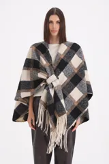 Mantela de tejido de punto con diseño de cuadros grandes en tonos negro, gris y beige. Presenta un cierre frontal con trabilla y terminaciones con flecos en el ruedo.