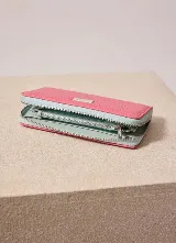Billetera de cuero sintético con cierre perimetral, color fucsia en el exterior y celeste en los fuelles, con placa metálica grabada con el logo de la marca.