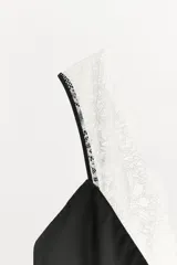 Vestido midi de satén negro con escote en pico y tirantes finos. Presenta detalles de encaje blanco a contraste en el escote y en el ruedo.