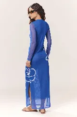 Vestido largo de malla azul traslúcida con estampado de flores blancas, cuello alto y mangas largas. Tiene aberturas laterales en el ruedo.