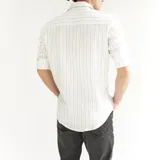 Camisa de algodón a rayas verticales celestes y grises claros, con cuello italiano y botones marrones.