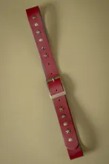 Cinto de cuero color rojo con hebilla metálica rectangular y apliques decorativos en forma de estrellas y tachas circulares metálicas.