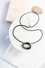 Collar con cordón negro y dije circular plateado de acero quirúrgico.