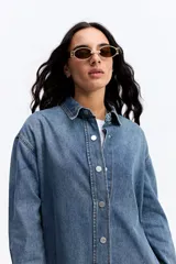 Vestido tipo camisa de jean con calce holgado, cuello clásico, cierre frontal con botones y ruedo con terminación desflecada.