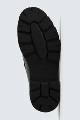 Mocasín negro de cuero liso con antifaz y flecos en el empeine. Presenta costuras blancas visibles y suela track gruesa de goma.