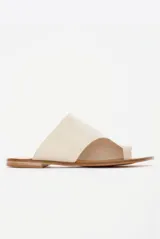 Sandalias chatas de cuero color off-white, con diseño minimalista de tira ancha asimétrica y presilla para el dedo.