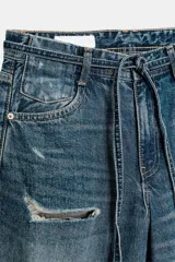 Jeans de tiro medio y corte baggy con cinco bolsillos, trabillas y rotos decorativos. Cuenta con detalle de cinturón confeccionado en el mismo tejido y cierre frontal con cremallera y botón metálico.