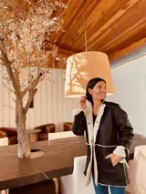 Gamulán negro con interior de corderito blanco, cuello alto, cierre frontal con broches y bolsillos laterales. Presenta tajos a los costados para mayor movilidad.