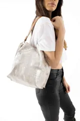 Bolso tipo shopper de cuero con acabado metalizado en tono plateado, con correa de hombro en color suela y herrajes metálicos.
