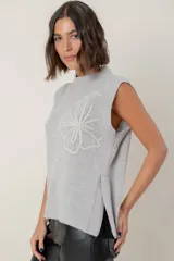 Chaleco de lana color crema con diseño de flor bordada en relieve en el frente, cuello redondo y aberturas laterales en el ruedo.