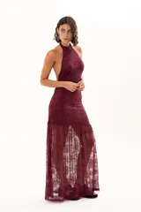 Vestido largo de encaje color bordó, con escote halter y diseño ajustado en el torso que se extiende hasta la cintura, donde continúa con una falda larga de encaje transparente.