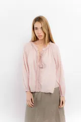 Blusa rosa de algodón con escote en V y mangas largas abullonadas con puños elásticos. Presenta detalle de volados en el escote y cordones con borlas para ajustar.