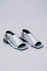 Sandalias plateadas de cuero con puntera cuadrada abierta, talón descubierto, tira trasera con hebilla y taco cuadrado bajo color negro.